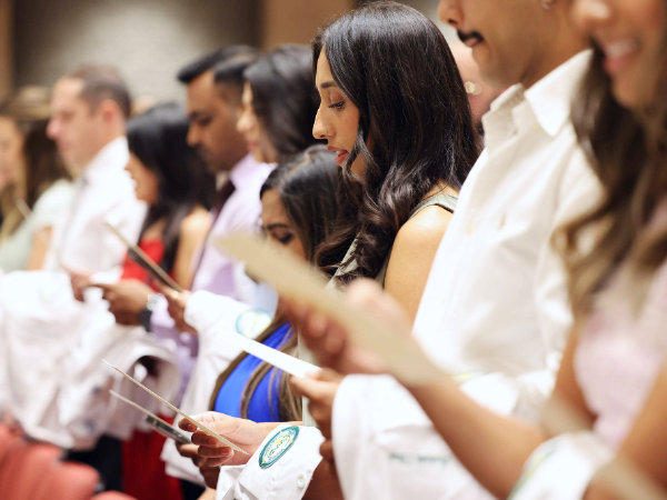 Various dental students with white coats draped over their arms reading from The Dentist's Pledge