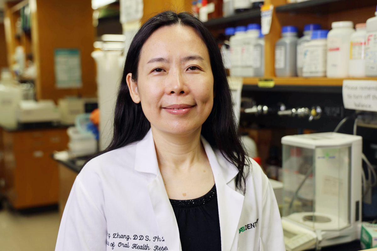 Image of woman with black hair in a white lab coat in a lab setting