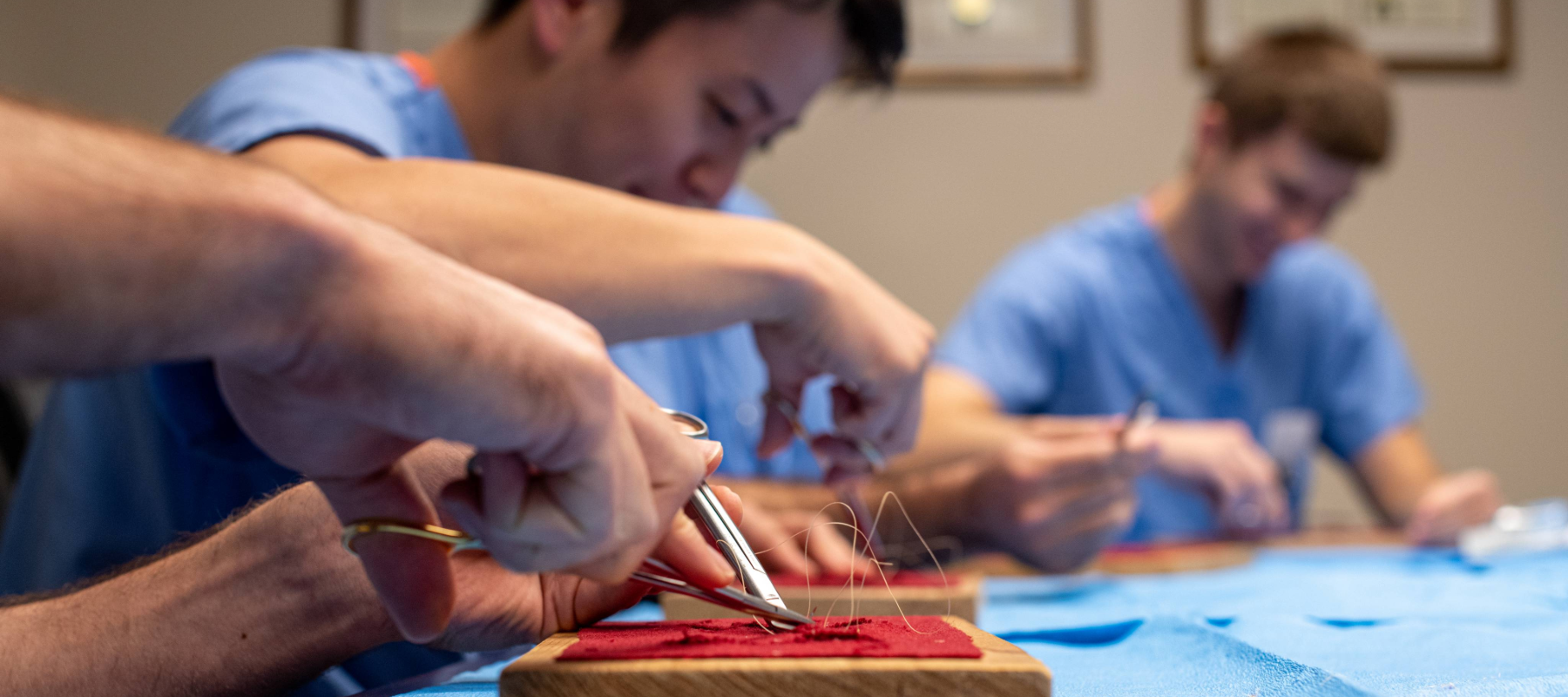 Oral surgery resdients in blue scrubs practicing suturing on fabric squares