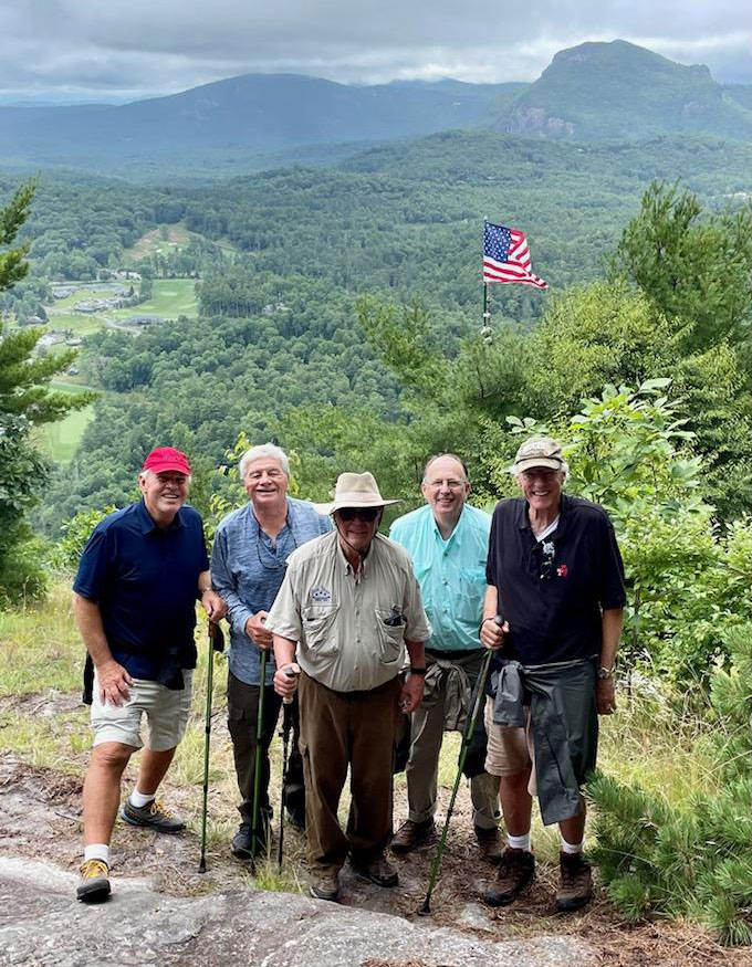 Five members of the class of 1972 posing in front of an American flag 72, trees and mountains in the background.