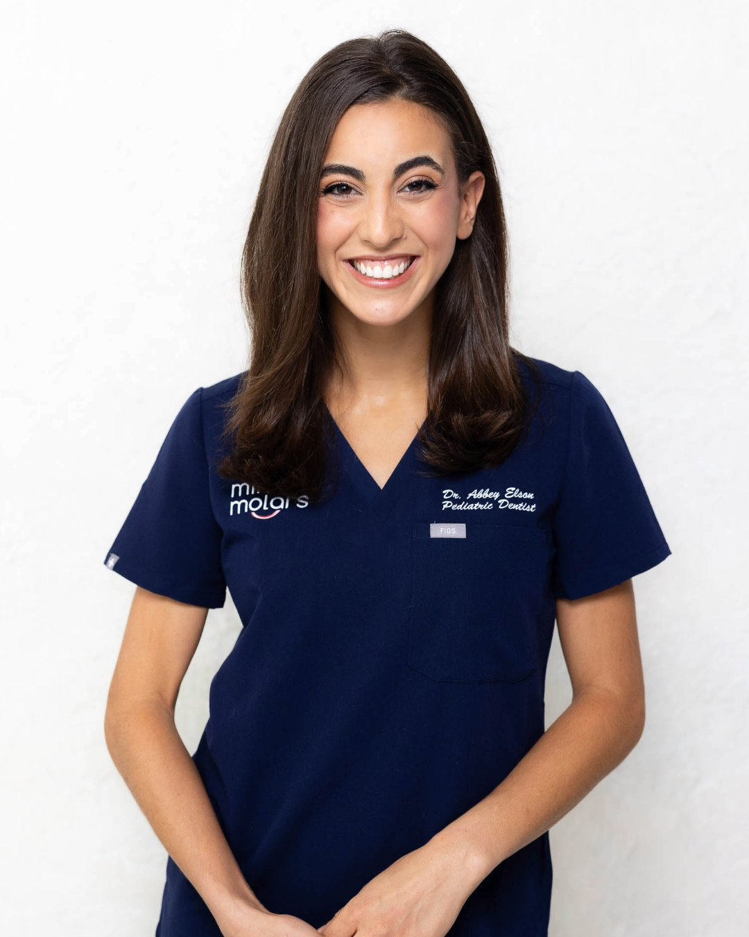 Woman in dental scrubs smiling for photo against white background