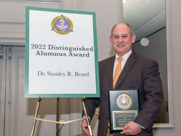 Dr. Stanley Beard holds his award and stands next to a poster announcing his win. 