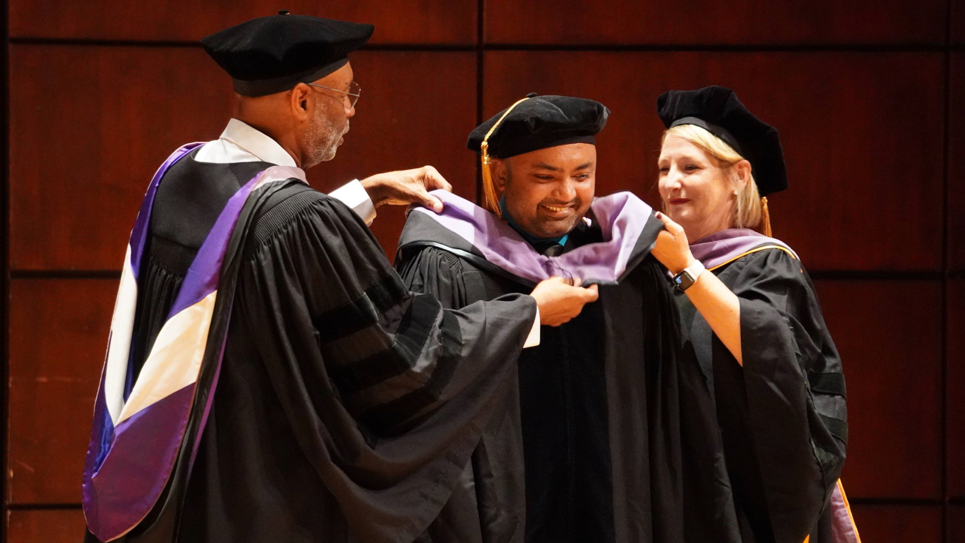 Student receiving hood from two faculty at 2024 DMD Commencement