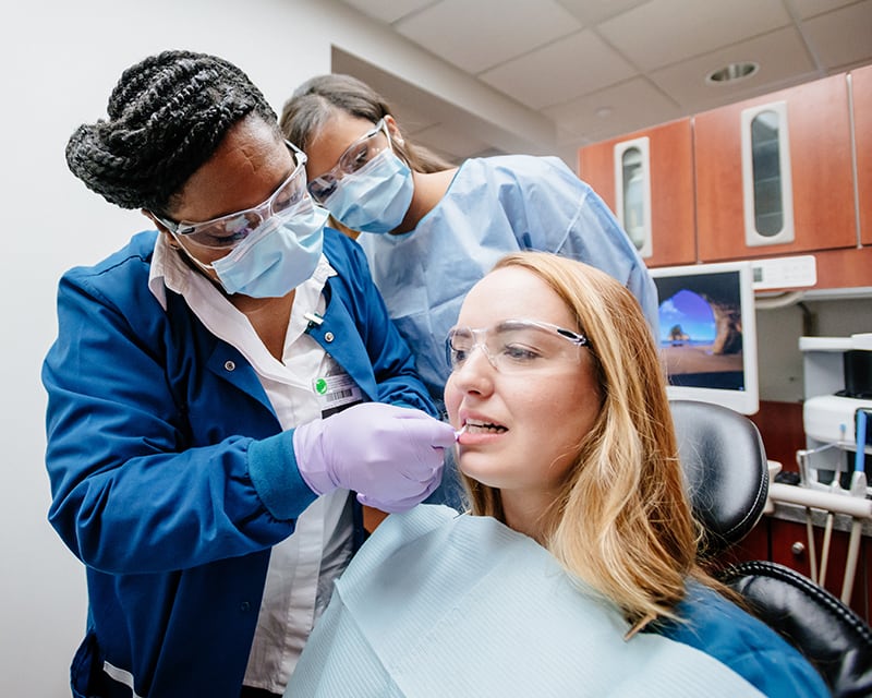 One woman flossing a patient's teeth, while another woman observes.