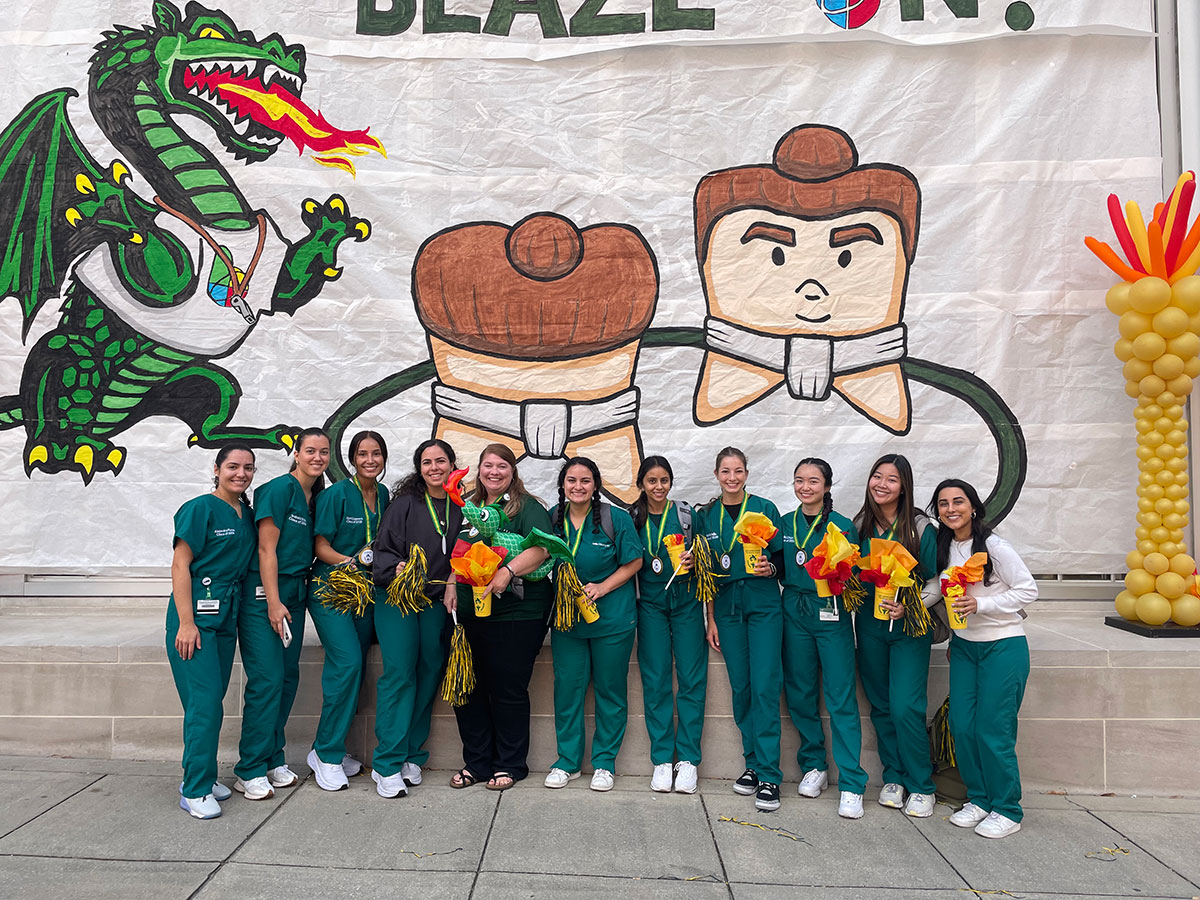Dentistry students at UAB homecoming in front of banner, holding swag. 