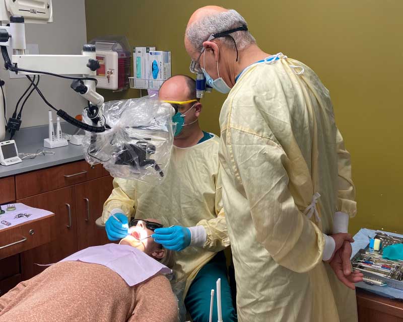 A person in scrubs performing dental procedure with another person observing.