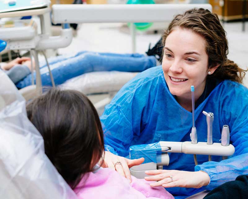 Dentist talking to young patient and gesturing  toward her mouth.