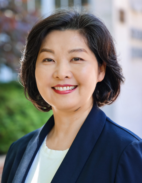 Woman with brown hair and eyes wearing professional attire smiling for photo in front of UAB School of Dentistry building and greenery