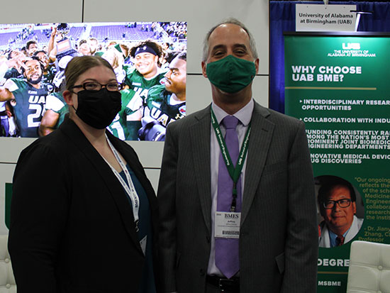 A faculty and student posing in the UAB booth wearing facemasks.