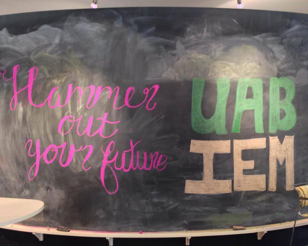 A photograph of a chalkboard with 'Hammer Our Your Future, UAB IEM' written on it.