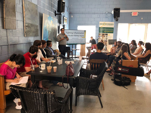 Crowd of students drinking coffee and listening to lecture.