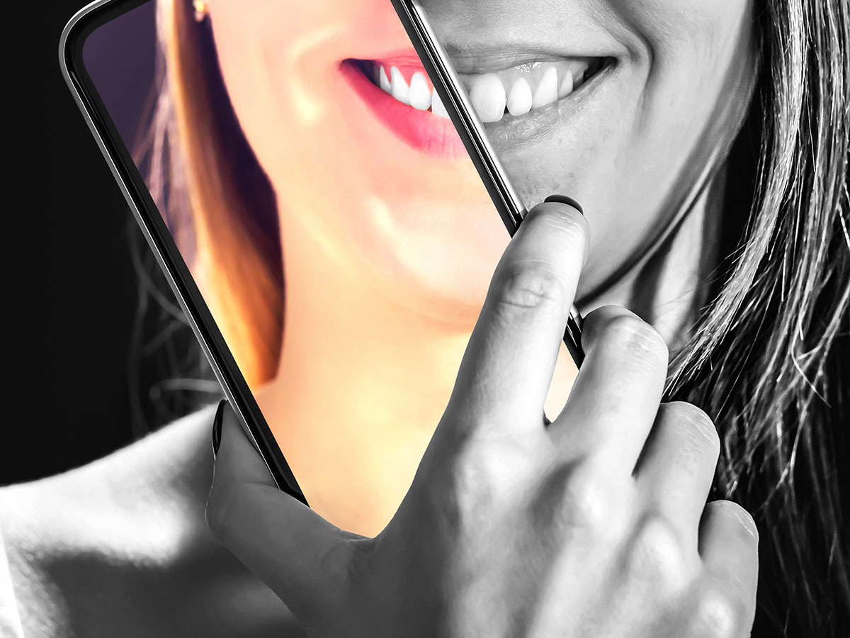 A young woman in black and white holds a phone up to her face, where her face is displaying in color. 