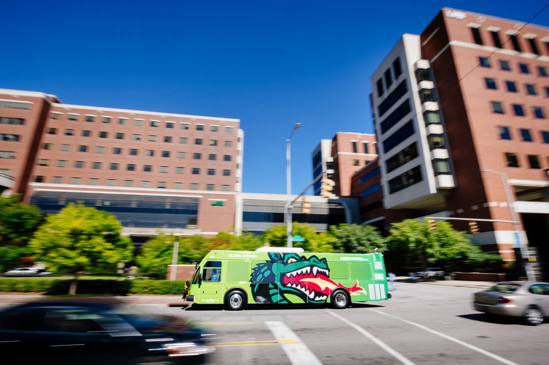 The Blazer Express shuttle bus colored lime green with a giant Blaze mascot logo on its side. 