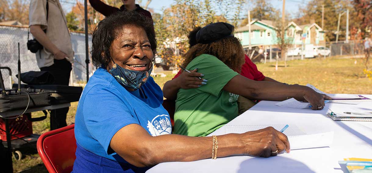 An older black woman smiles at the camera as she sits at a table.