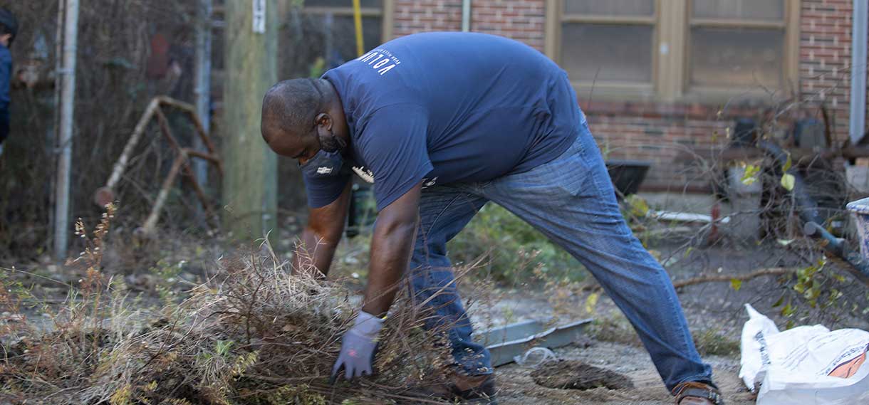 A Black male volunteers pulls weeds.