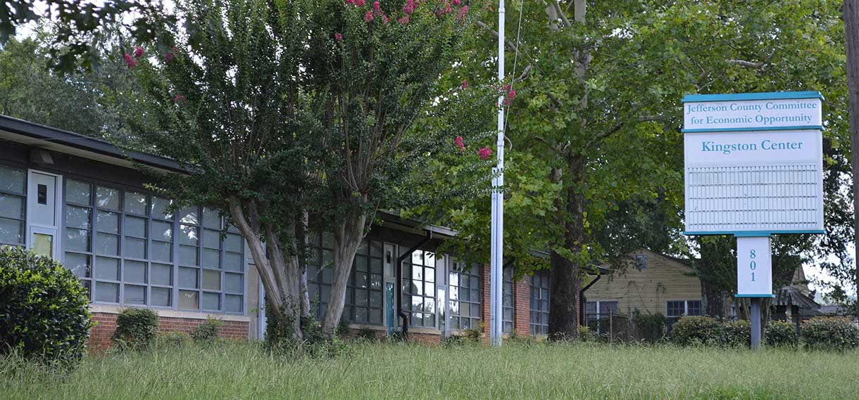 The Kingston Center with a sign, flagpole, and large pink crepe myrtle.