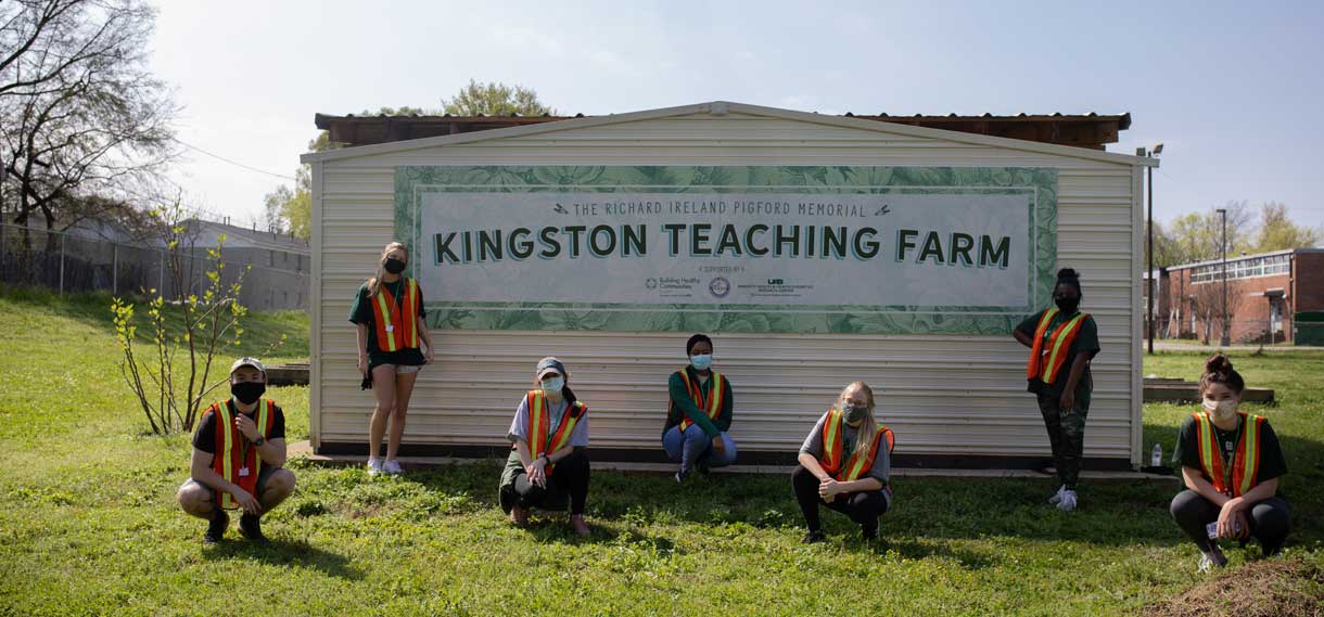 Volunteers in front of the Kingston Teaching Farm sign.
