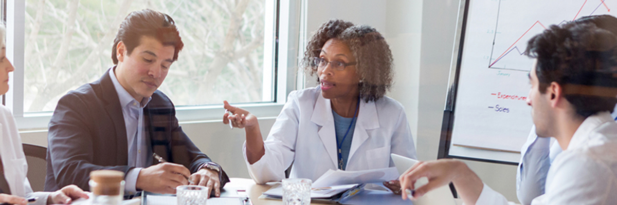 Mature female doctor gestures while discussing something during a healthcare conference with colleagues.