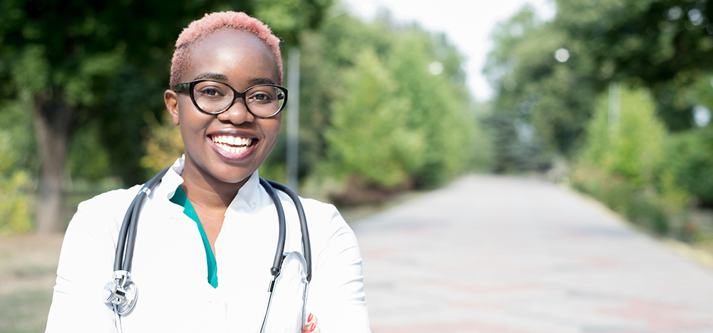 portrait of a young black girl, a doctor. Woman in a white coat, smiling, wearing glasses, with a stethoscope. Outdoor in