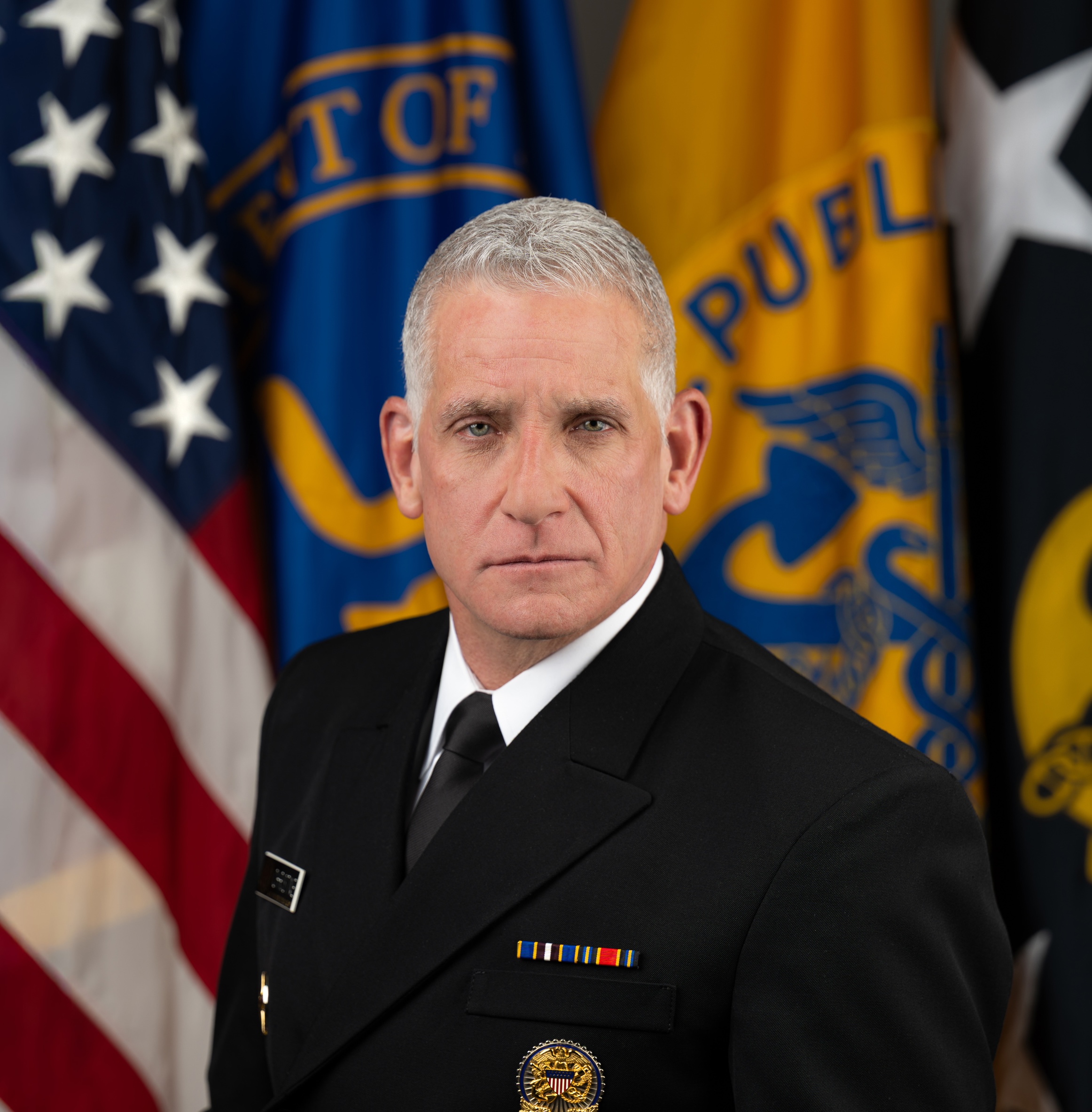 Portrait of Admiral Brian Christine, M.D., sitting in front of the American flag in a black suit.