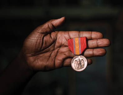 An african american woman's hand holds a National Defense Service Medal. 