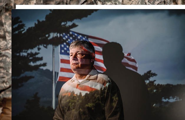 An image of Pete Lane, D.O., gazing to the left as an image of an American flag is projected over the scene. The projected image appears both on the white of the subject's shirt, and on the background behind him. 
