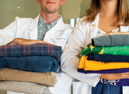 Two medical students pose with stacks of folded, donated clothes. 