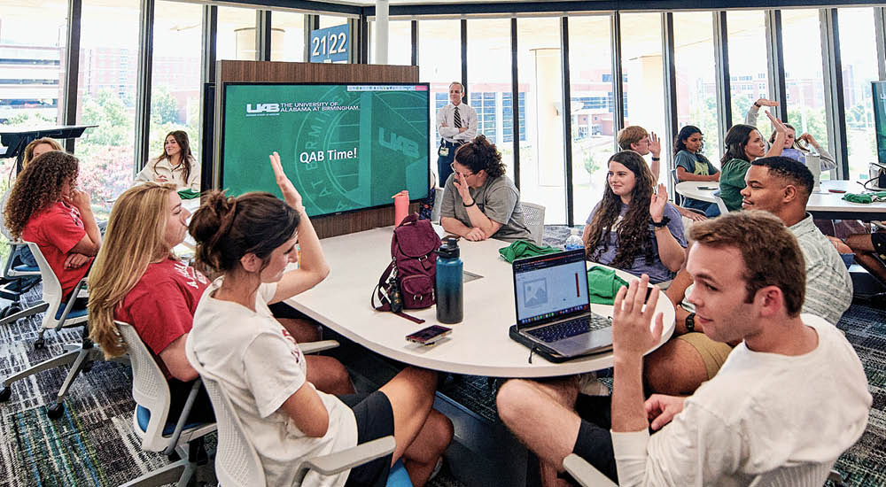 Students attending class in the learning center. Five students are seated around a table with a large screen which reads "Q&A Time". 