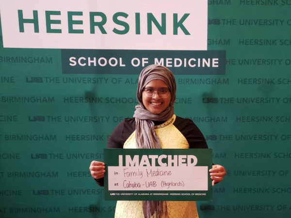 Medical student poses with an I matched sign in front of the school of medicine logo