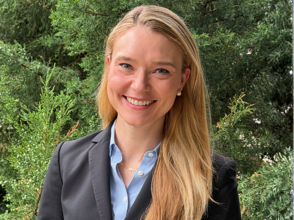 Smiling woman wearing a dark suit with greenery in the background
