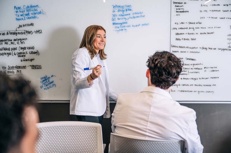 Several medical students (one smiling) are collaborating and using dry erase board