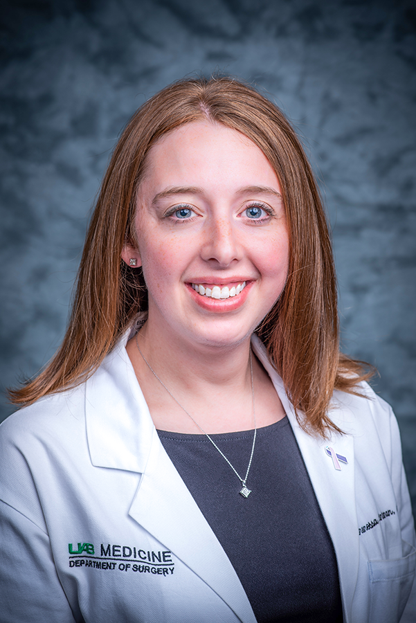 Headshot of Dr. Brenessa Lindeman, associate professor in the Department of Surgery. Dr. Lindeman, wearing a blue-ish gray shirt and white coat, is smiling against a blue backdrop.