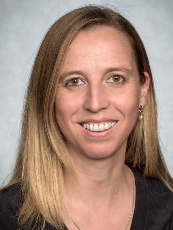Andrea Comba, Ph.D., stands in front of a gray background.