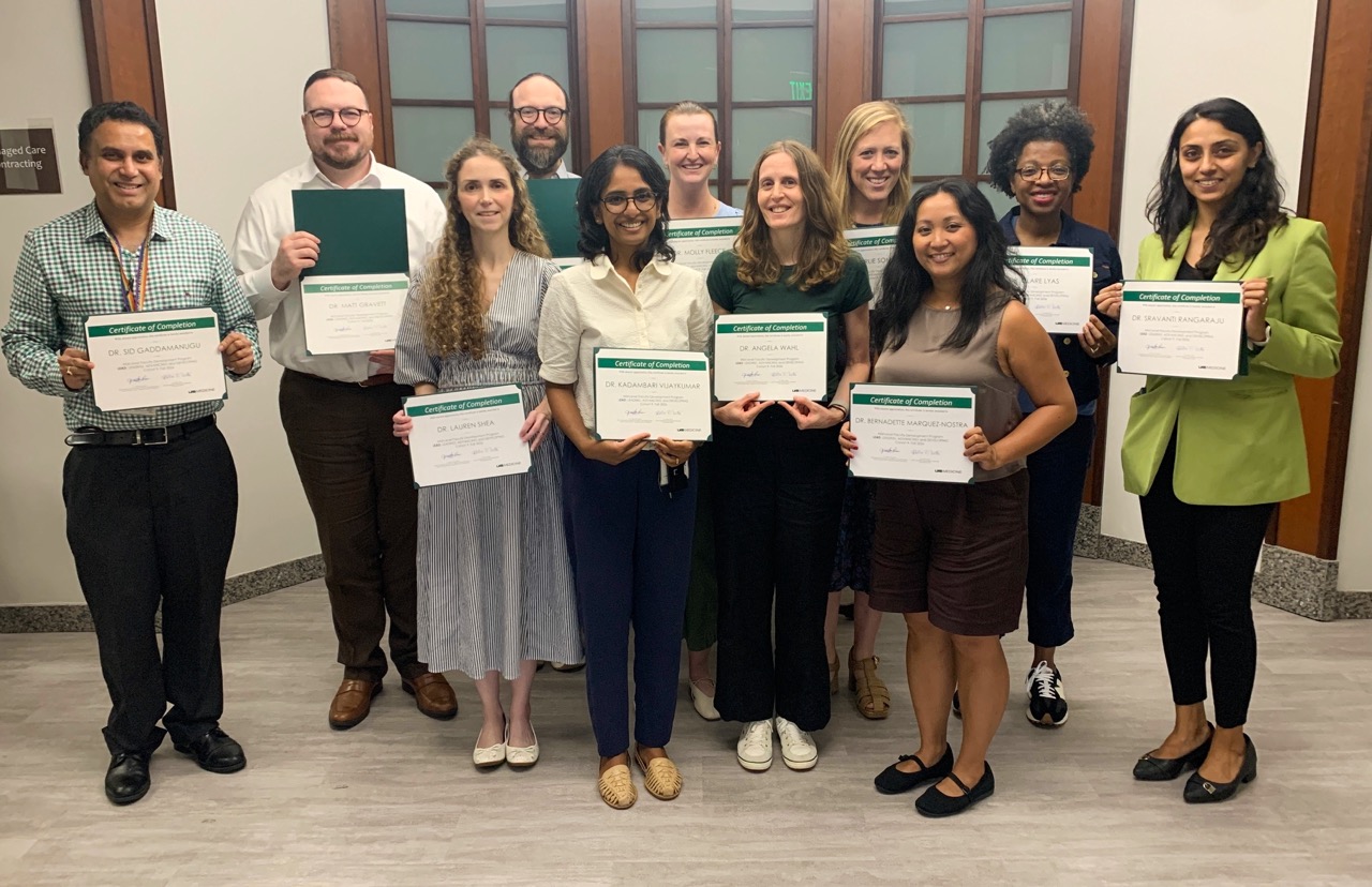 Group of faculty and staff holding certificates of completion and posing for a photo in a hallway.