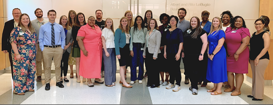 Group of 24 professionals posing together and smiling in a modern office lobby.