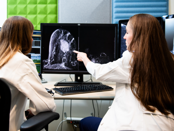 Two physicians reviewing imaging on a computer with backs turned towards the camera. One is pointing out something on the imaging.