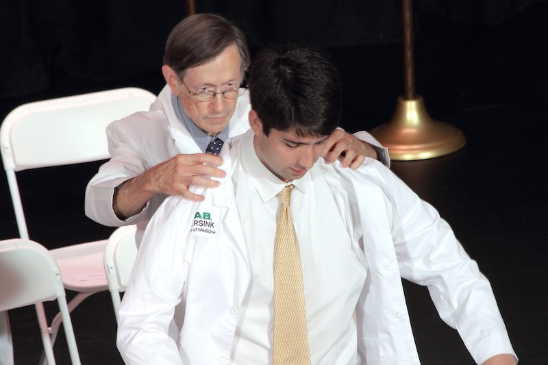 Medical student putting on white coat on stage.
