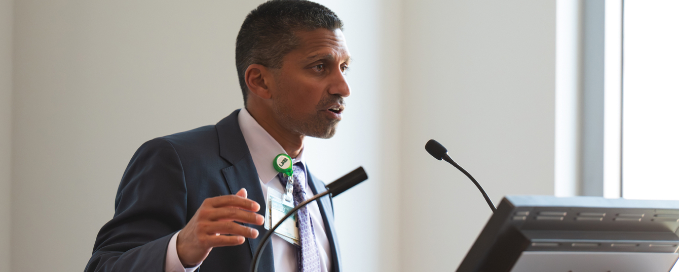 Irfan Asif speaking at a podium in the Marnix E. Heersink Institute for Biomedical Innovation Conference Center.