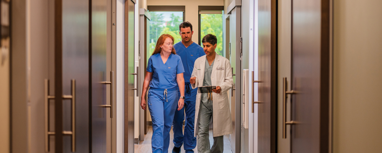 Orthopedic surgeon Amit Momaya, M.D., and two nurses walk and talk in a hallway in the UAB Sports and Exercise Medicine Clinic.