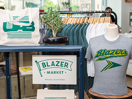Blazer Market at Yellowhammer Creative store at Pizitz Food Hall. Close-up of UAB Blazer-themed tote bag, and t-shirt  on mannequin form on display in store, 2019.