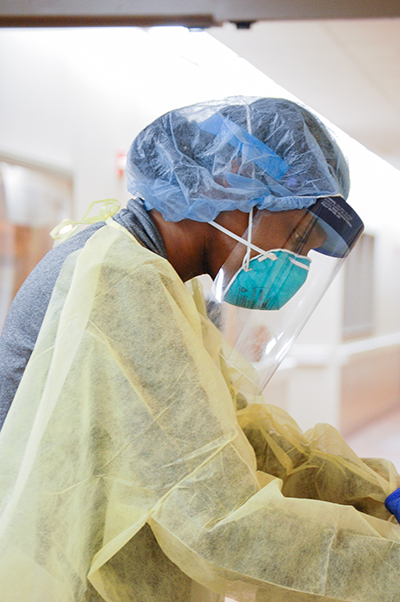 From side, black female nurse is wearing Personal Protective Equipment (PPE) while working in the Hospital during the COVID-19 (Novel Coronavirus) pandemic, March 2020.