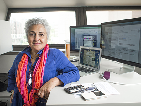 Environmental shot of Dr. Haydeh Payami, PhD (Professor, Neurology) standing in front of computer monitors at her desk, 2015.