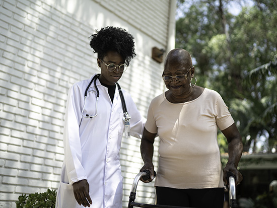 Home caregiver helping senior woman to walk