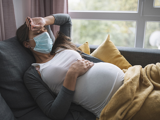 Pregnant woman with protective face mask laying sick at home.