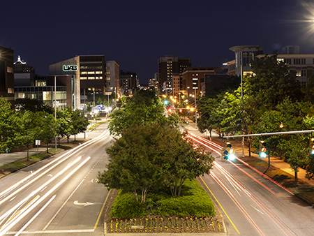 Shot from pedestrian bridge, view of University Boulevard at night showing campus buildings on either side of the street and in the background, May 2020.