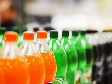 A long line of unbranded soda bottles in various flavours and colors, the focus on the center of the line.