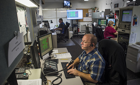 From side, three people are working at Birmingham Regional Emergency Medical Services System (BREMSS) in the UAB Trauma Communication Center, 2016.