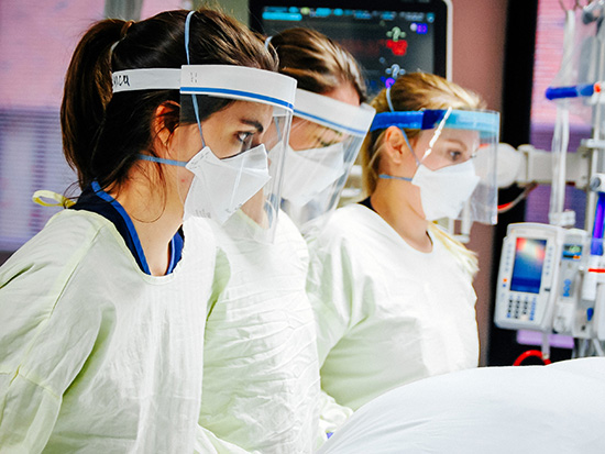 From side, Adriana Sharples, RN (Registered Nurse, Medical Nursing), Grace Marett, RN (Registered Nurse, Medical Nursing), and Meghan Kelly (Certified Respiratory Therapist, Respiratory Care) are wearing PPE (Personal Protective Equipment) face shields, face masks, and gowns while proning a COVID-19 patient being treated at UAB Hospital for COVID-19 (Coronavirus Disease), December 2020.