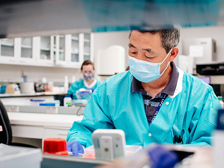 An unidentified Asian man is wearing a PPE (Personal Protective Equipment) face mask and gown while working in the UAB Genomic Diagnostics Laboratory (GDL), located in the West Pavilion, during the COVID-19 (Coronavirus Disease) pandemic, April 2021.