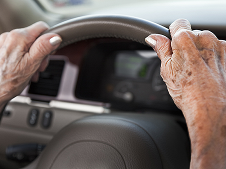 Senior woman driving car with hands on steering wheel.